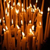 About 30 slender white candles, lit against a dark background